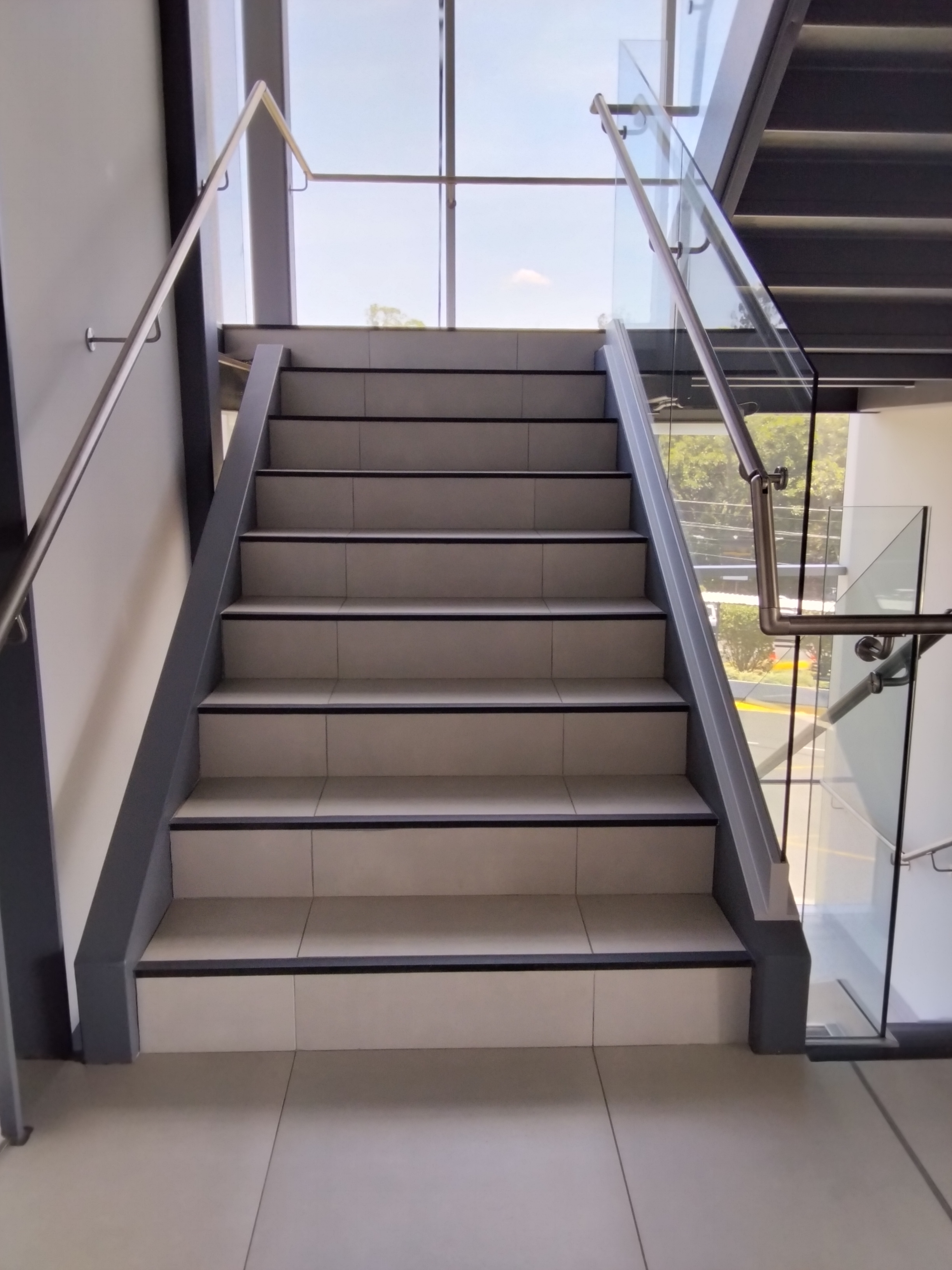 A modern staircase featuring light gray tiles, leading up with smooth edges and a stainless steel handrail.