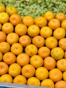 
A close-up view of a vibrant display of oranges stacked closely together, showcasing a variety of shades of orange with some minor imperfections on their skin.