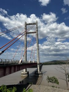 
A view of a suspension bridge with red cables arching across a river. 