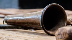 A close-up, angled studio photograph of the bell section of a vintage brass instrument resting on a wooden surface.