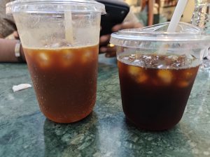 Two iced tea drinks in clear cups with ice cubes—one light and fizzy, the other dark and rich, both refreshing.
