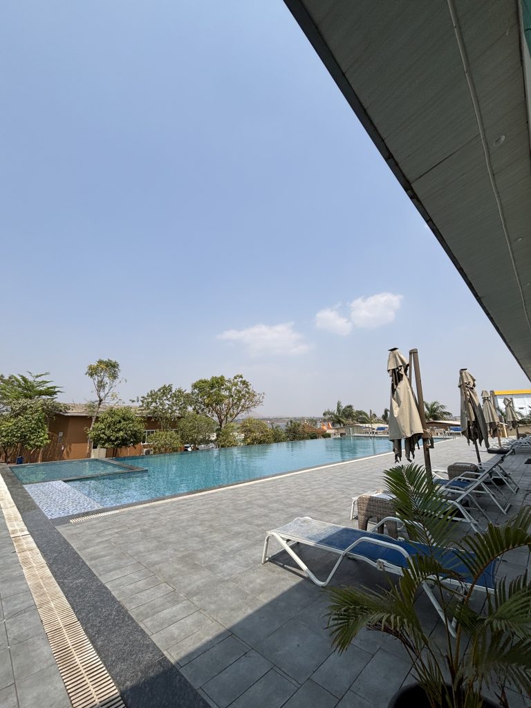Outdoor infinity pool with lounge chairs and umbrellas under a clear blue sky.
