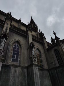 Aged Gothic church facade with pointed arch windows, stone statues, ornate spires, and weathered stonework under an overcast sky.