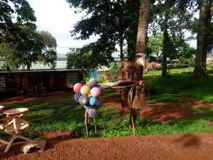Colorful woven balls and handmade items including wire frame locally crafted toy cars displayed outdoors in a grassy area with trees.