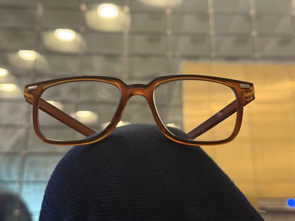 A pair of brown eyeglasses is resting on a person’s knee, with a blurred background featuring soft, circular light reflections and textures