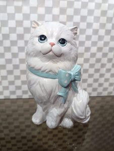 A ceramic figurine of a fluffy white cat with large blue eyes and a small pink nose. 
