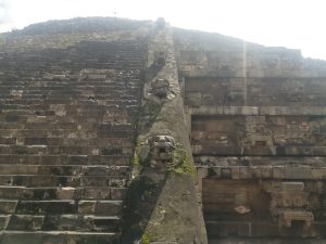 A close-up view of a stone pyramid structure featuring several stepped levels. The left side displays a series of worn stone steps leading upwards, while the right side showcases intricately carved stone reliefs, including faces and decorative patterns. México