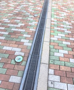 A close-up view of a textured pavement made of interlocking bricks in various shades of brown, green, and gray
