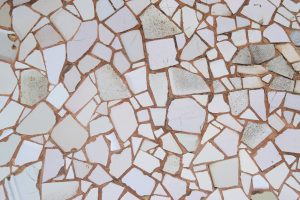 Close-up of a broken ceramic tile mosaic pattern with white and beige fragments and brown grout.