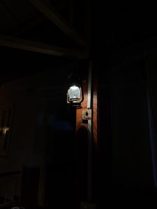A vintage lantern is mounted on a wall, casting a soft glow in a dimly lit space. 