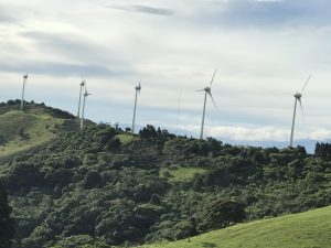 Wind turbines rising above green hills, creating a striking contrast between modern energy and the natural landscape.