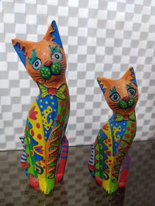
A pair of colorful, decorative figurines of cats are displayed on a reflective surface. 