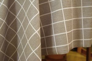 A close-up view of a grey fabric tablecloth with a white square grid pattern, draped in soft folds.