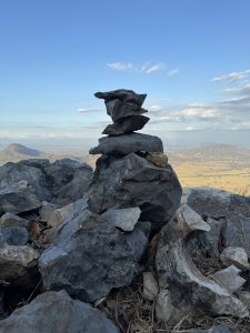 Stacked rocks forming a small cairn on a mountain viewpoint with a scenic landscape in the background.