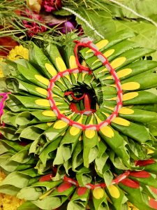 A colorful arrangement of green leaves and yellow petals tied with red thread at Shree Siddhivinayak Temple, Bandra, Mumbai. The close-up shows fine details and traditional design in a vibrant way. 
