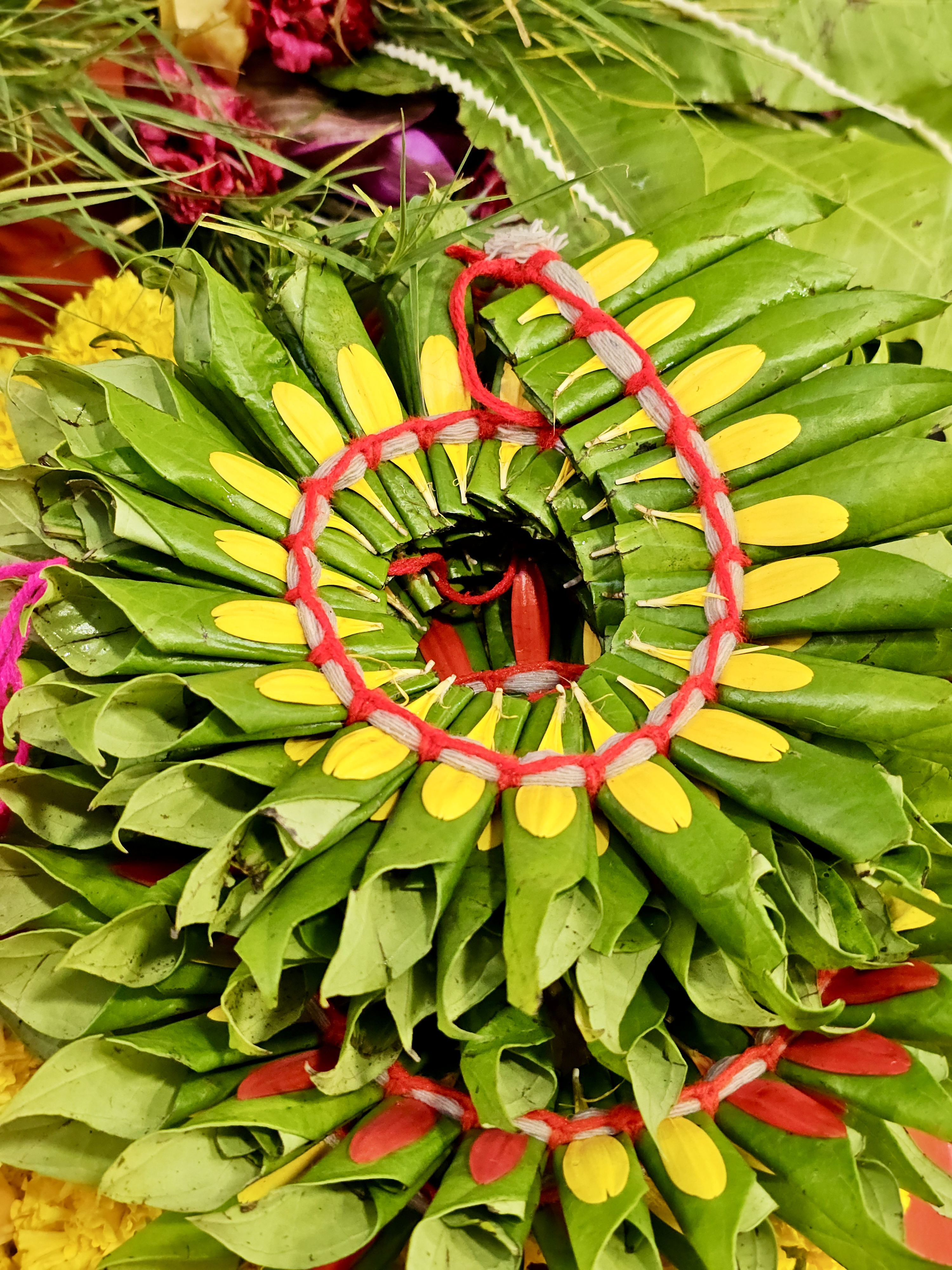 A colorful arrangement of green leaves and yellow petals tied with red thread at Shree Siddhivinayak Temple, Bandra, Mumbai. The close-up shows fine details and traditional design in a vibrant way.