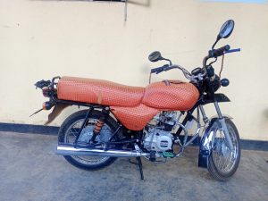 A motorcycle with a brown patterned seat parked on a concrete floor against a cream wall.
