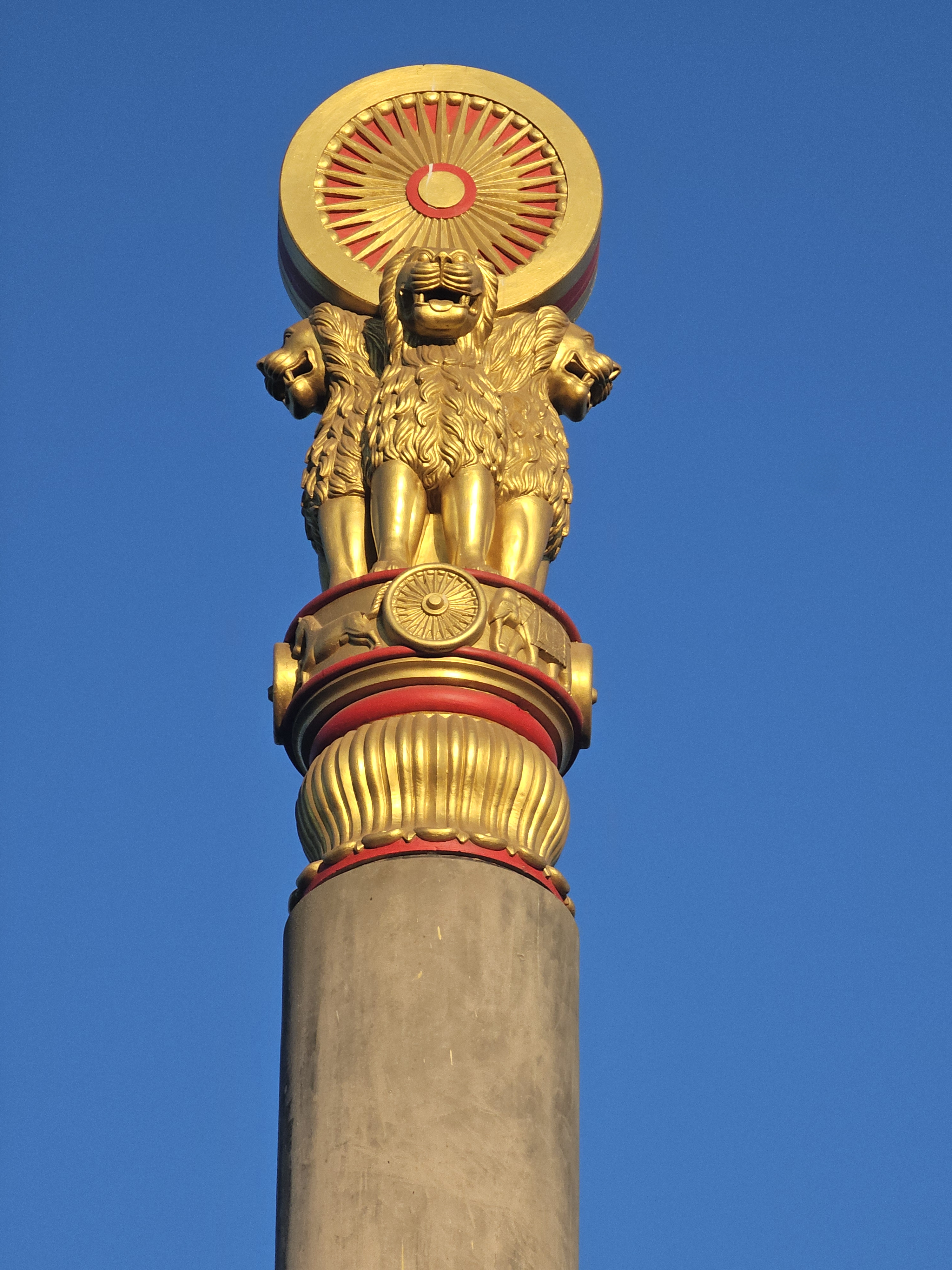 A close-up of the Ashoka pillar with three lions and a wheel symbol, shining in golden color against the blue sky at Global Vipassana Pagoda, Gorai Village, Mumbai.