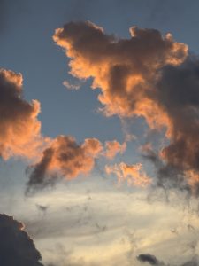 Clouds illuminated by the sunset with warm orange and golden tones against a partially cloudy sky.