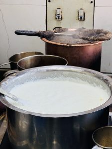 A large pot of steaming milk with a wooden ladle, and another boiling tea pot in the background.