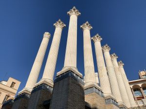 A close-up of ancient Roman-style columns in the Roman Temple of Córdoba, Spain, against a clear blue sky.