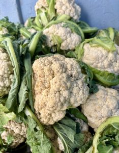 
A close-up view of several heads of cauliflower, surrounded by leafy green stems. 
