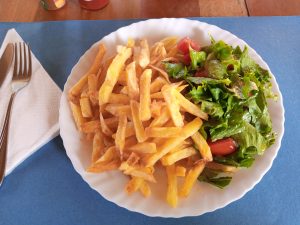 A white plate holds a serving of golden, crispy French fries alongside a fresh green salad with leafy lettuce and a few cherry tomatoes.