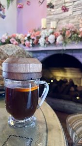 Smoked orange coffee in a glass mug with a wooden lid, with a cozy fireplace in the background.