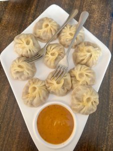 A plate of dumplings served with a side of dipping sauce.