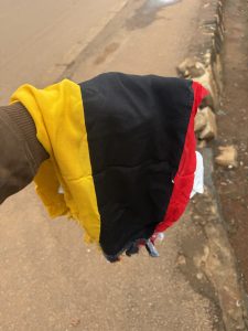 A hand holding out black yellow red scarf (Uganda flag)