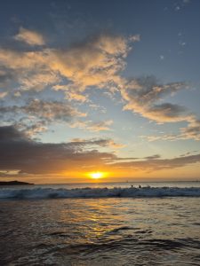 A serene beach scene at sunset, showcasing a vibrant sky with fluffy clouds tinted in shades of orange, pink, and blue. 