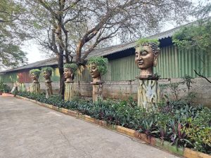 A row of decorative heads, resembling Buddha figures, are placed on stone pedestals along a pathway.
