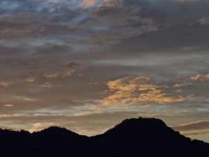 Silhouetted mountain peaks against a twilight sky with layered clouds in warm gold, orange, and purple hues.