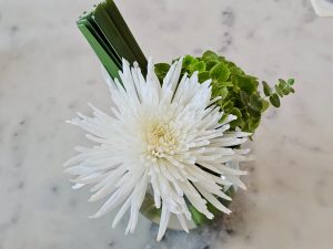 A fresh white flower arrangement in a small glass vase with green leaves, placed on a marble surface in Kurla, Mumbai. 