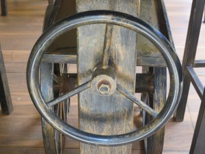 A black three-spoke handwheel mounted on a metal and wood table with a worn yellow-brown base.