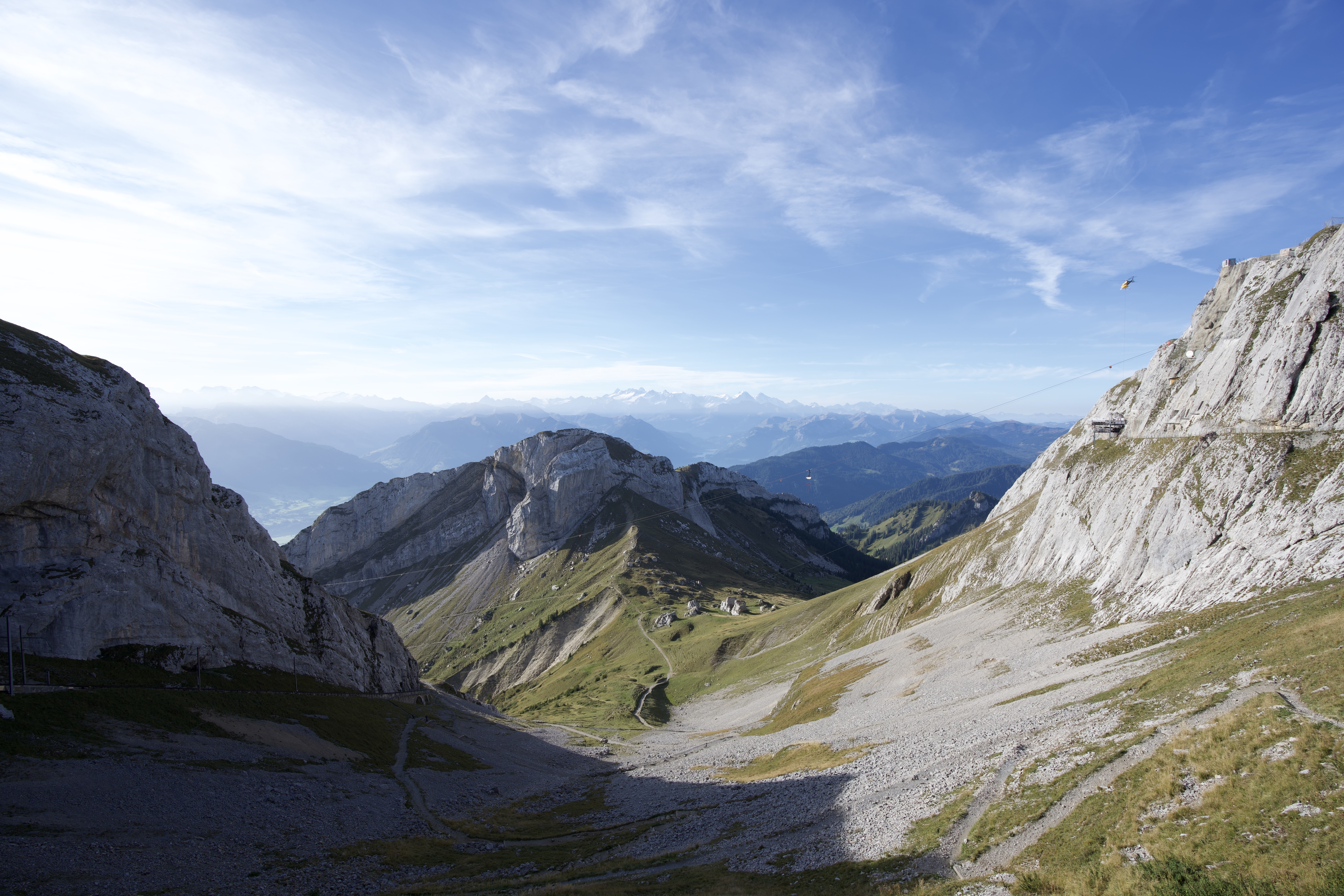 Swiss mountain range with rugged rocky peaks, green grassy slopes, and a clear blue sky in the background.