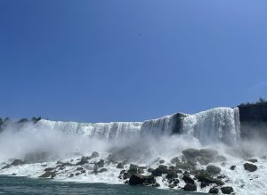 A large waterfall flowing over cliffs into a river with mist, under a clear sky at Niagara Falls in Canada