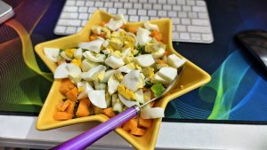 A top-down close-up of a yellow star-shaped bowl with egg, carrot, and cucumber salad, beside a keyboard and mouse.