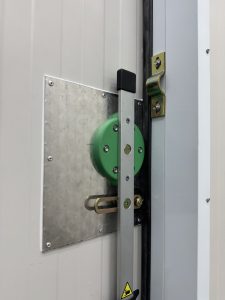 
A close-up view of a door mechanism, featuring a green pulley attached to a metallic plate