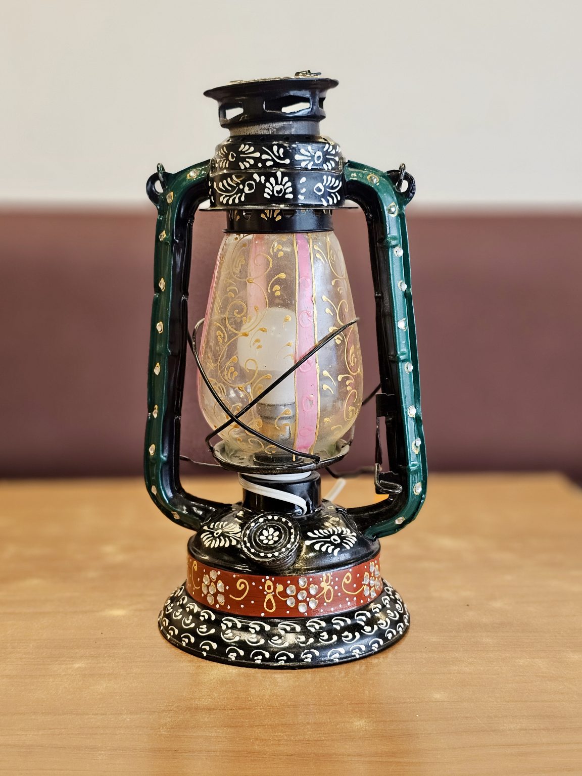 A vintage-style lantern (lamp) with painted designs placed on a wooden surface at Kurla, Mumbai. The soft background and centered frame make it look clean and attractive.