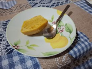 Half of an orange cupcake on a plate, and a spoon on its side.