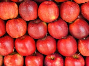A close-up view of numerous bright red apples stacked closely together, showcasing their shiny skins with hints of yellow and green near the stems.