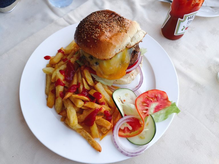 A cheeseburger with melted cheese and onions is served with chips, ketchup, and a fresh salad.