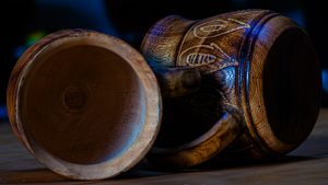 A close-up, high-angle photograph of a single hand-carved wooden spoon resting on a polished dark wood surface.