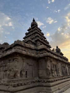 Ancient stone temple with intricate carvings and a stepped tower, viewed from a low angle against a soft sunset sky with scattered clouds.