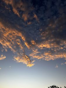 A sky filled with fluffy clouds at sunset, featuring shades of orange and gold contrasting against a deep blue backdrop.