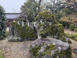 Kameishi (Tortoise Rock) at Achi Shrine in Kurashiki, Japan—a sacred moss-covered rock decorated with a shimenawa rope and paper streamers.
