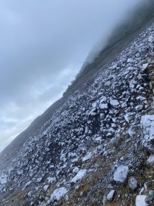 Rocky hillside with scattered stones and misty fog blending into green vegetation.
