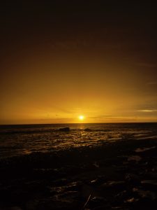 A serene beach scene at sunset, showcasing a vibrant orange and yellow sky transitioning into a darker horizon.