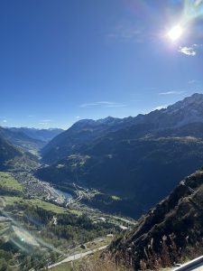 A simple mountain landscape with a clear blue sky, green valleys, and small villages below.
